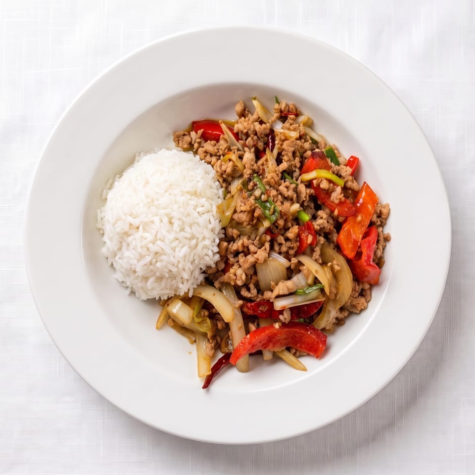 White plate with a serving of ground meat stir-fry, red peppers, onions, and white rice.
