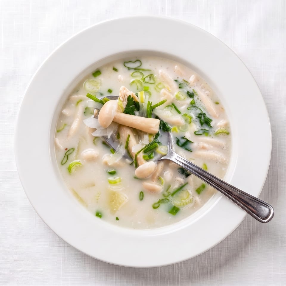 Creamy mushroom and noodle soup with green onions and a spoon in a white bowl.